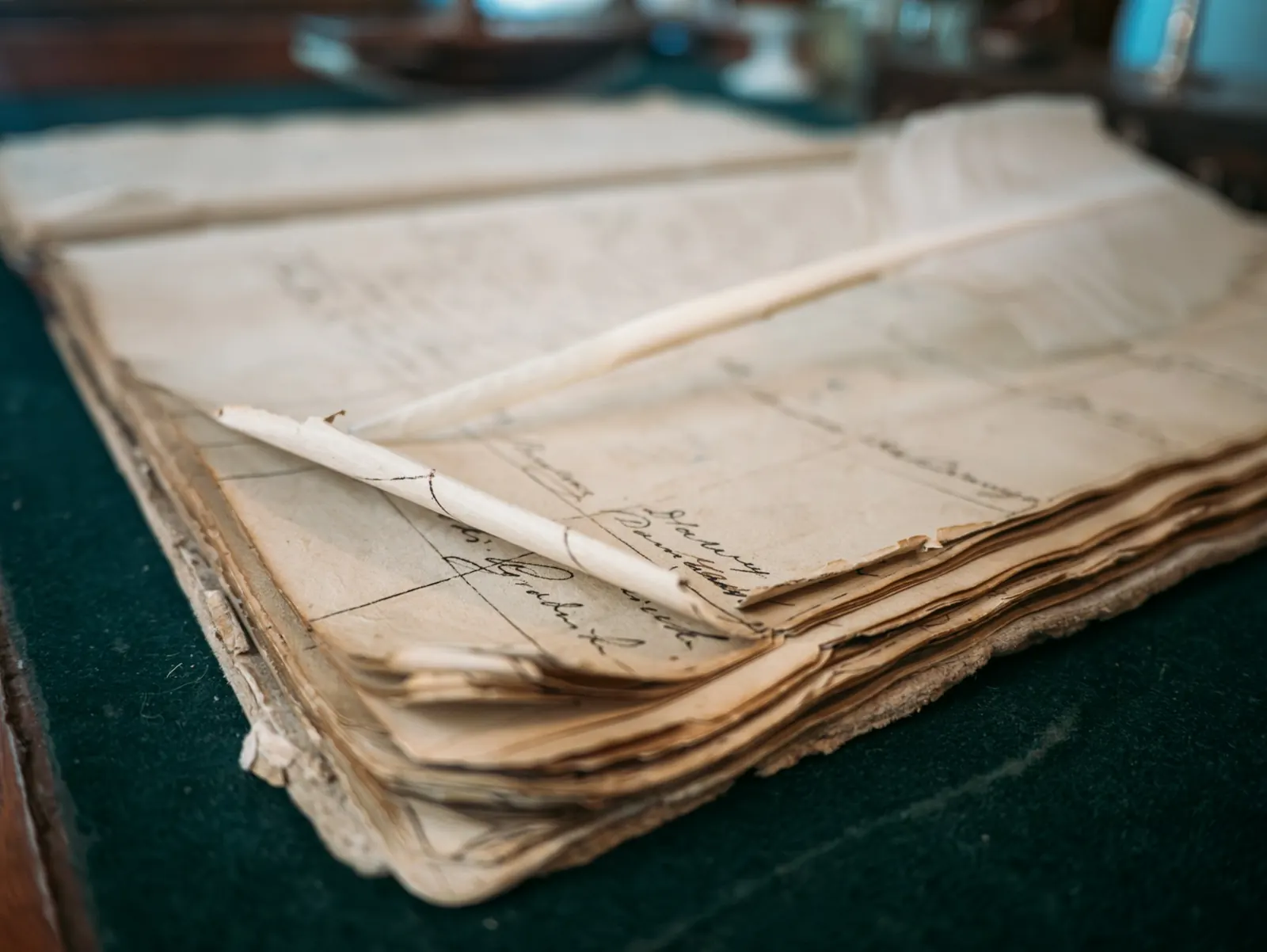 A worn ledger book open to ruled columns of handwritten entries, a pen resting across the page.
